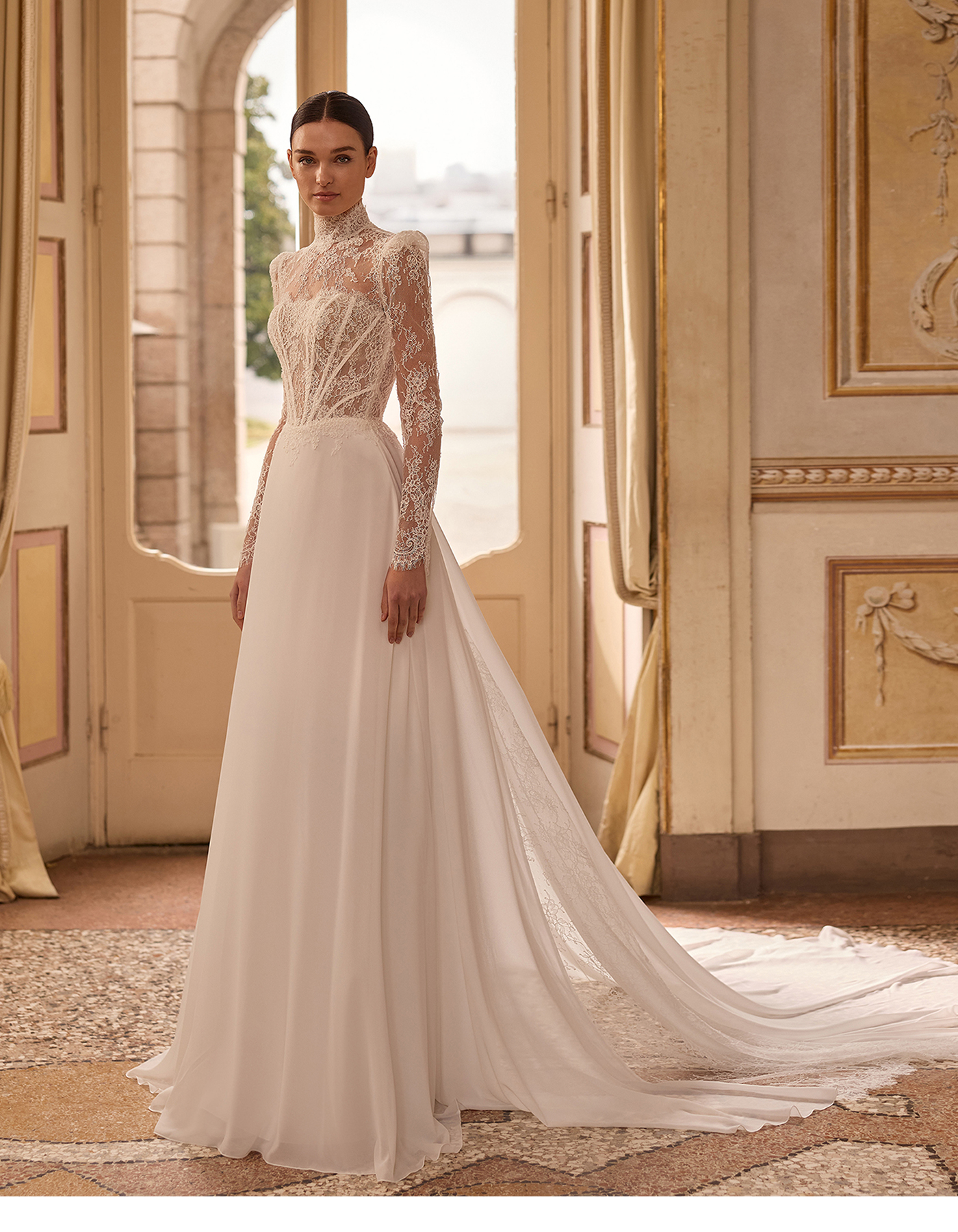 Bride in a high-neck lace wedding gown with a long train, standing in a sunlit ornate doorway.