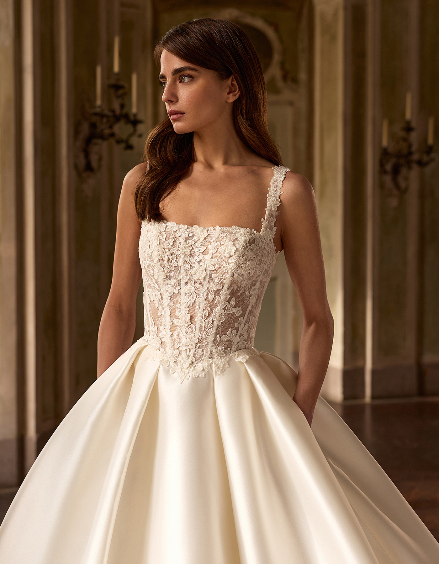Bride in an ivory lace wedding dress with a full satin skirt, standing in a grand hall.2?